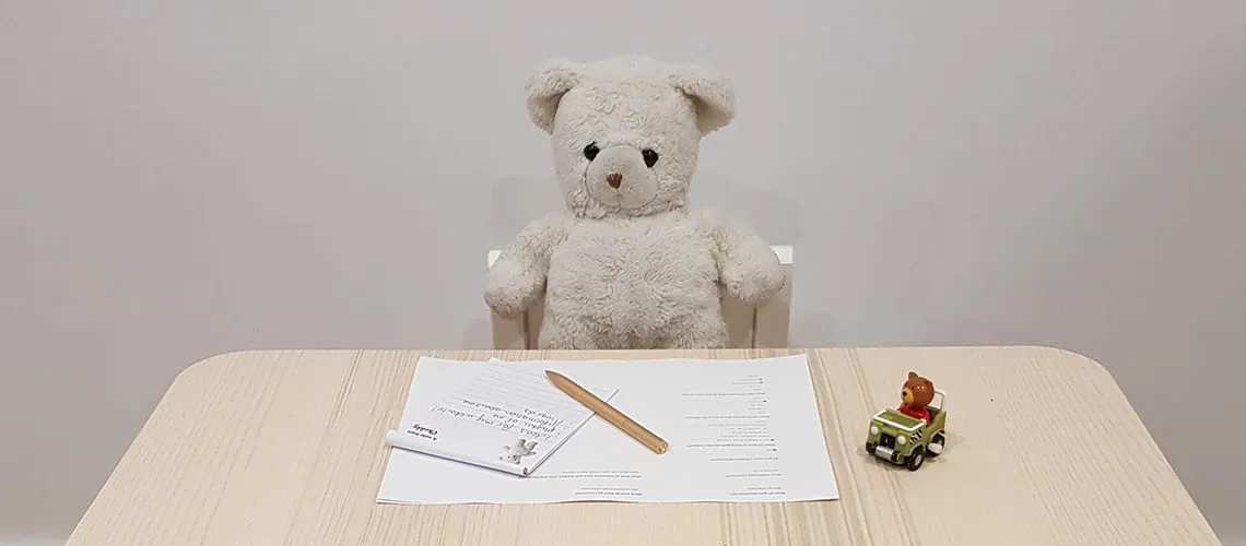 Teddy bear at desk with paper and toy car.